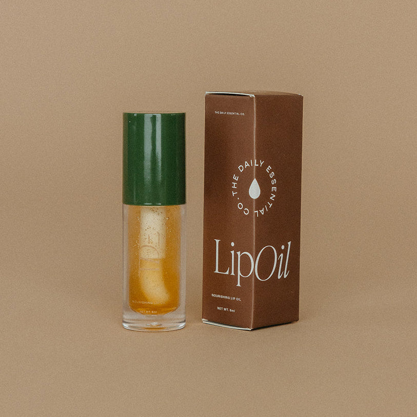 Lip oil with green cap and brown box on a beige background
