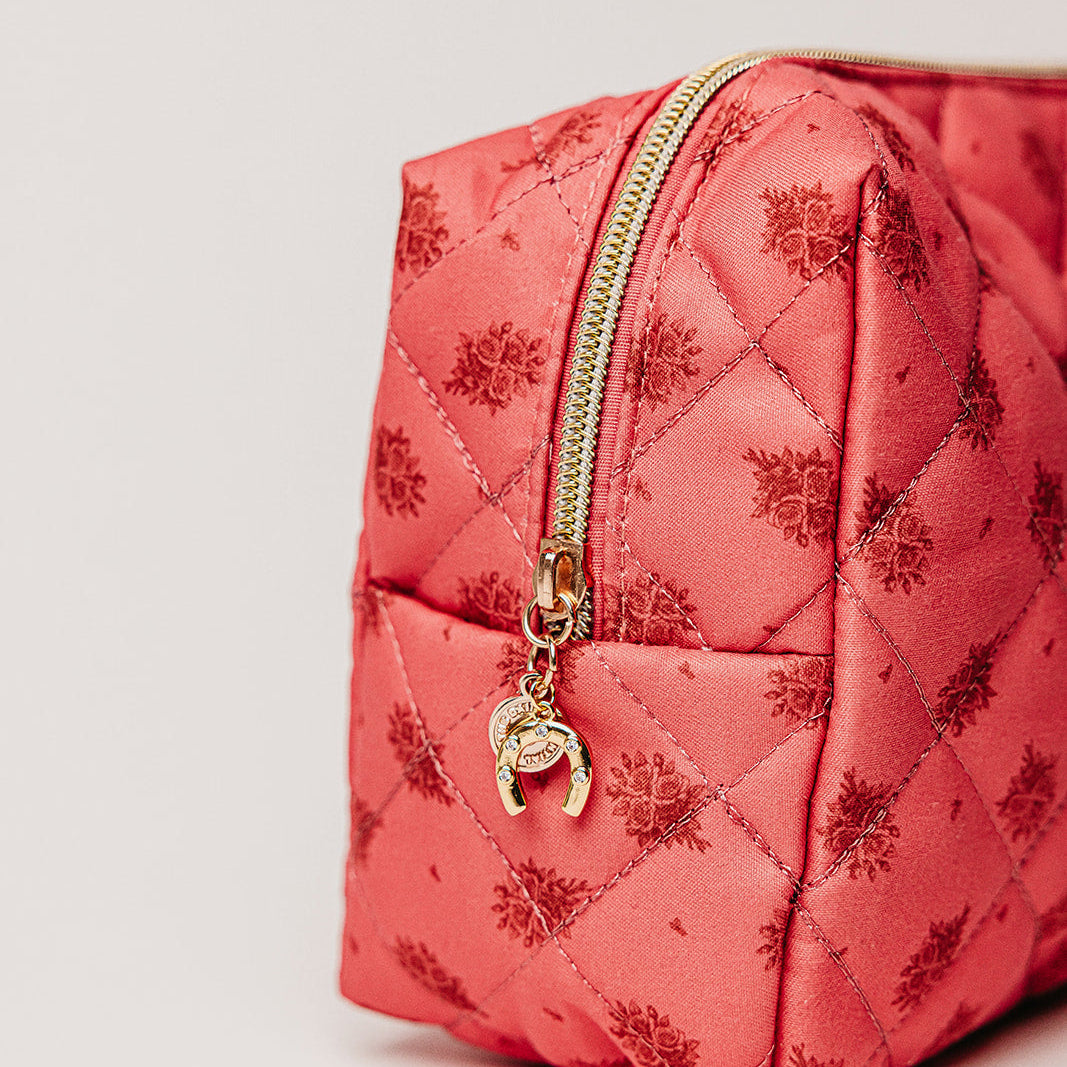 Pink quilted bag with gold zipper and charm on a light gray background