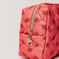 Pink quilted bag with gold zipper and charm on a light gray background